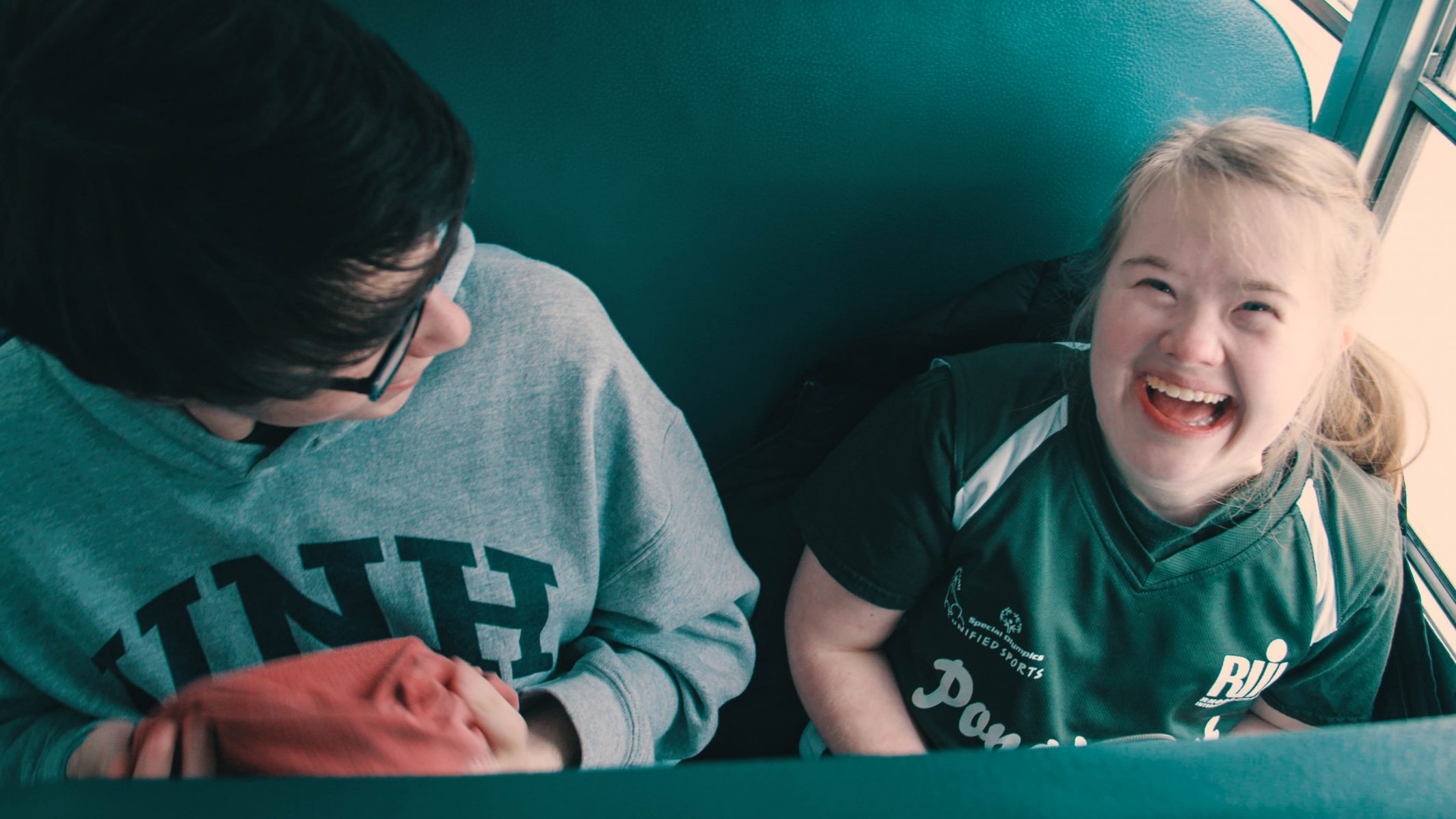 Kate DeCotis and a classmate sitting on the bus. Kate is smiling at the camera.