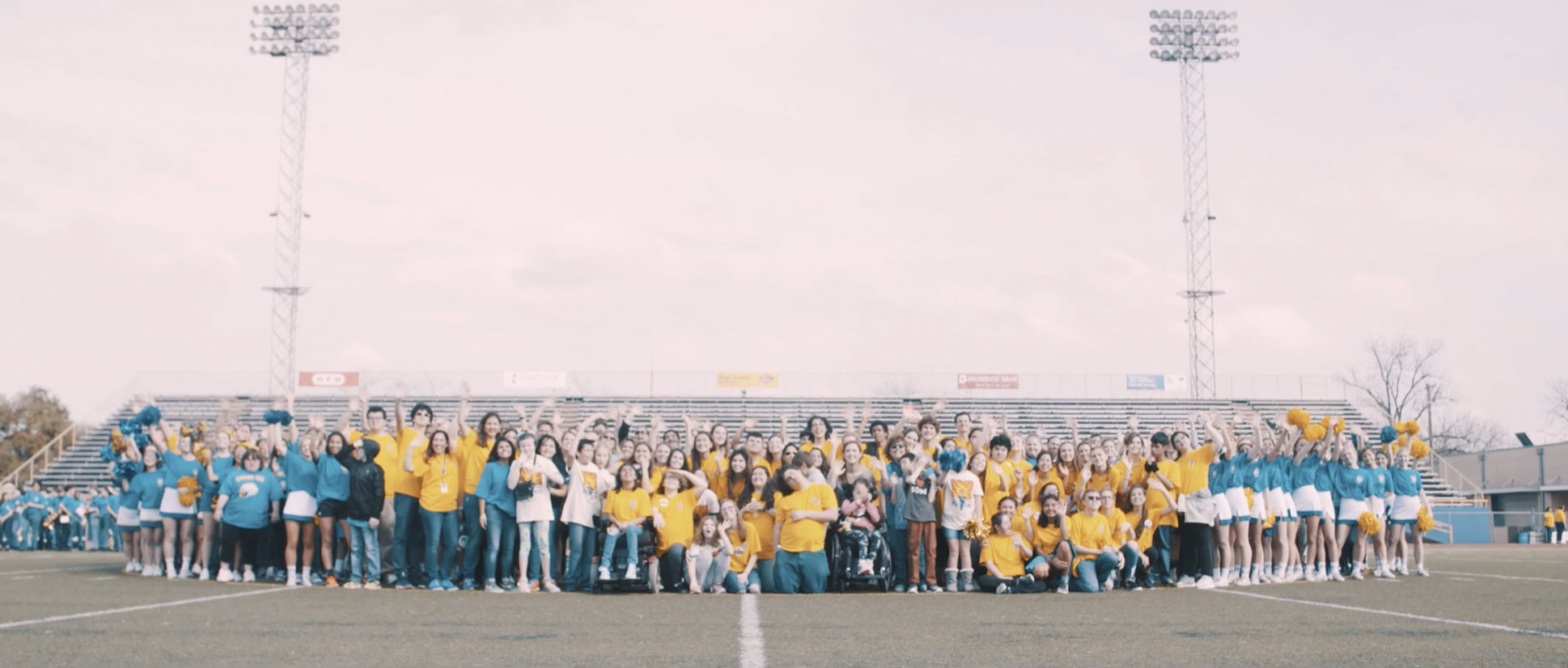 A group of students from Alamo Heights High School waving to the camera on a football field.