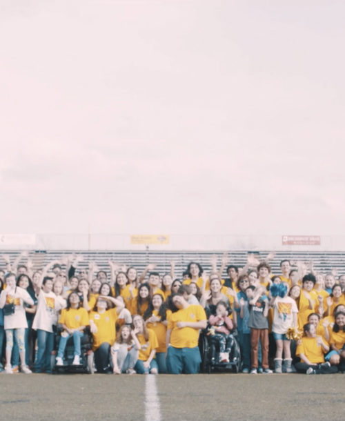A group of students from Alamo Heights High School waving to the camera on a football field.