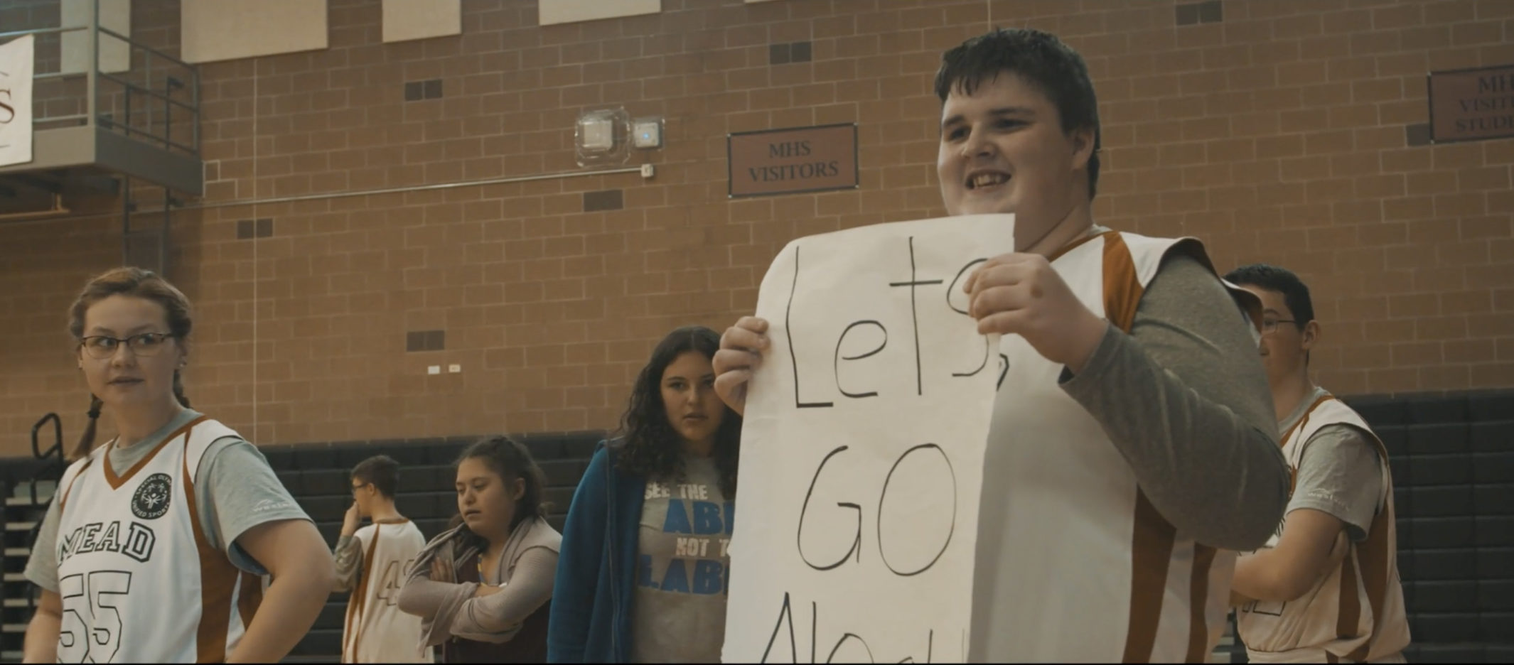 Noah from Mead High School smiling as he holds a sign that says 