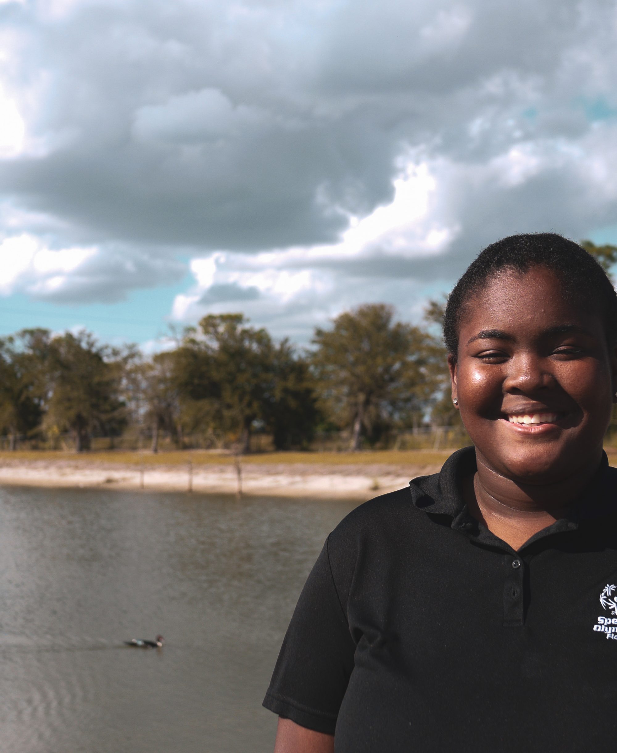 Tajha, a US Youth Ambassador from Florida smiles for the camera while standing in front of a lake.