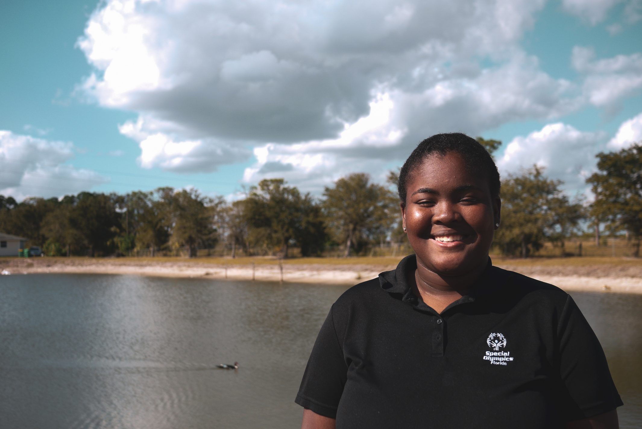 Tajha, a US Youth Ambassador from Florida smiles for the camera while standing in front of a lake.