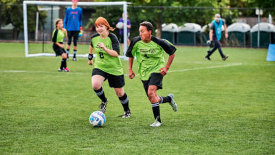 Two soccer players working together to dribble the ball down the field.