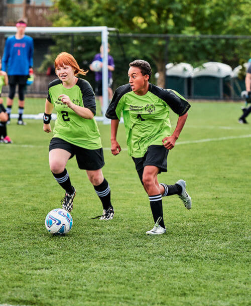 Two soccer players working together to dribble the ball down the field.