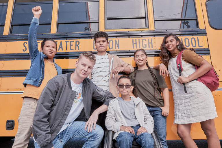 Group of students posing in front of a school bus.