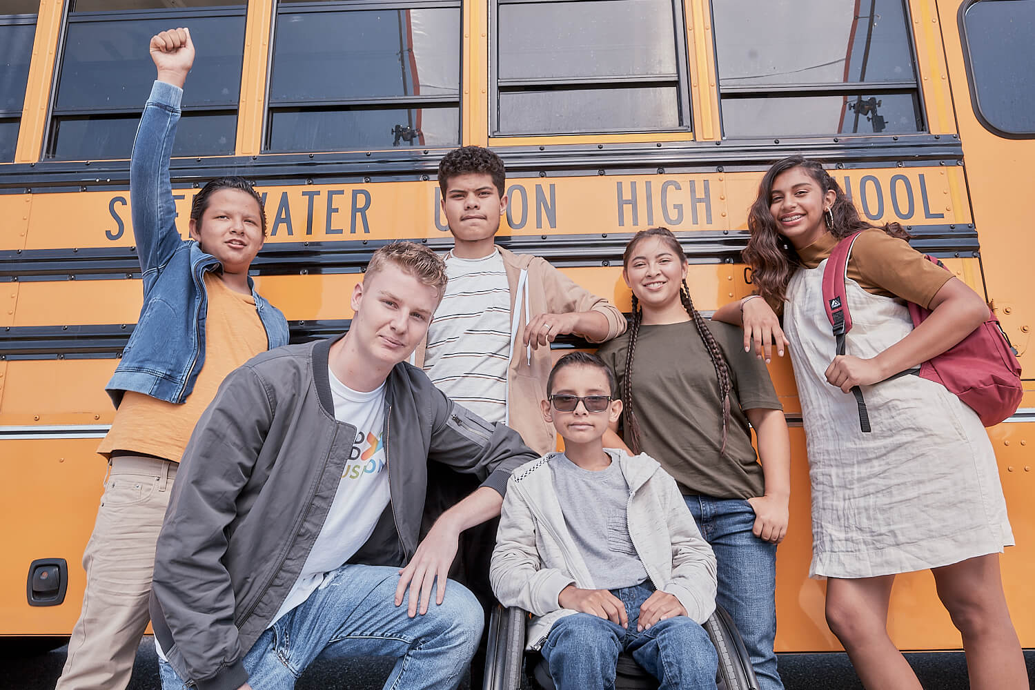 Group of students posing in front of a school bus.