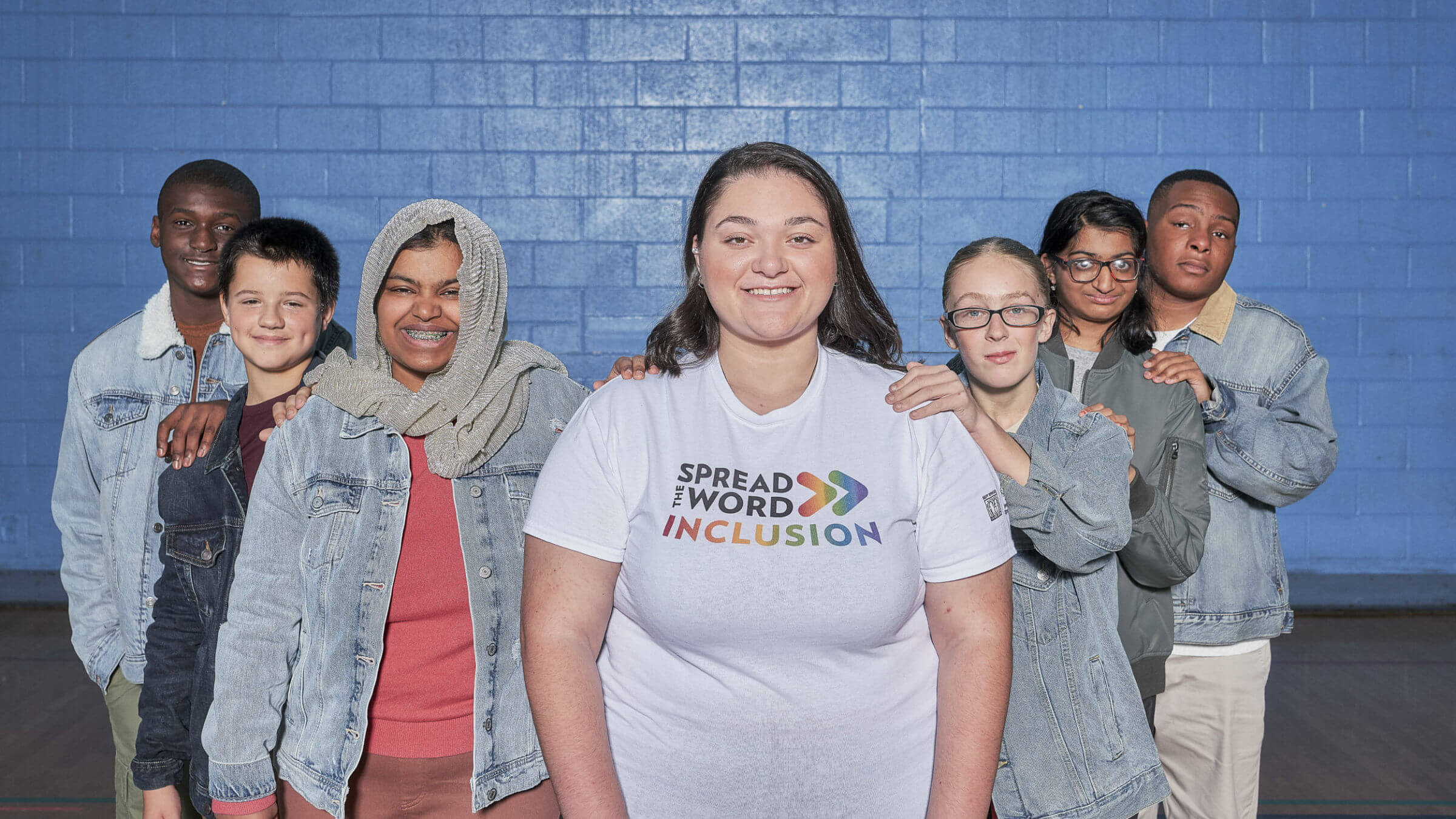 Group of students posing around one student wearing a Spread the Word shirt.