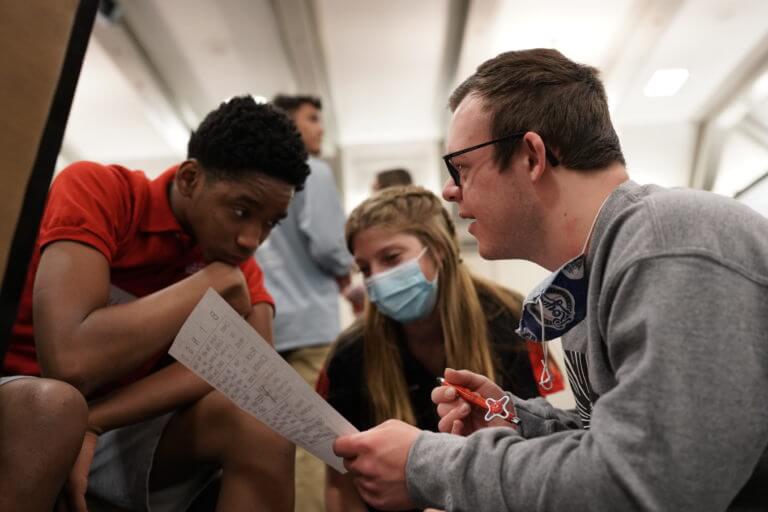 U.S. Youth Ambassadors Isaiah and Daniel working with a youth leader from Special Olympics Utah. They are crouched around a piece of paper.