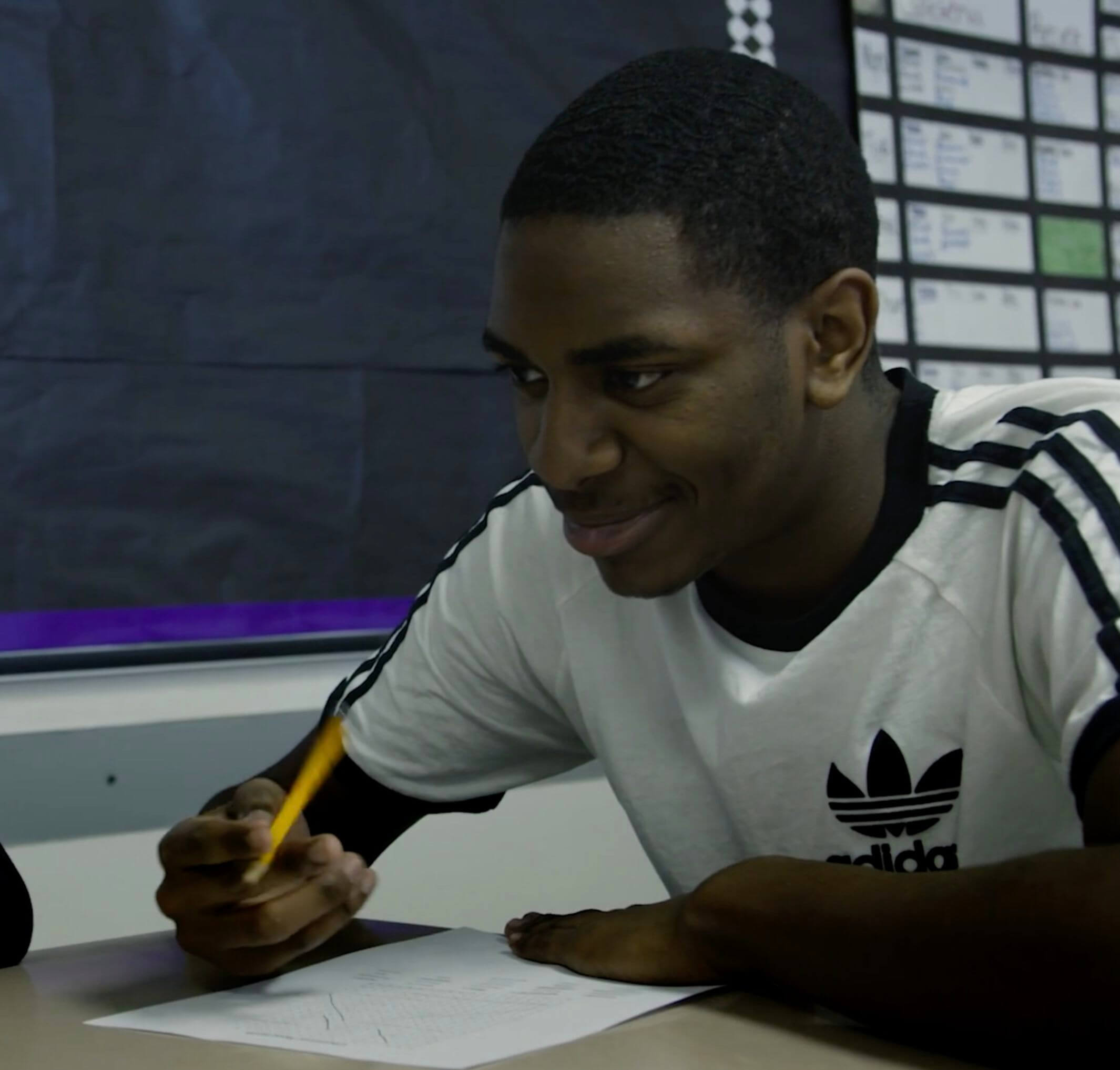 A student holding a pencil, smiling in class.