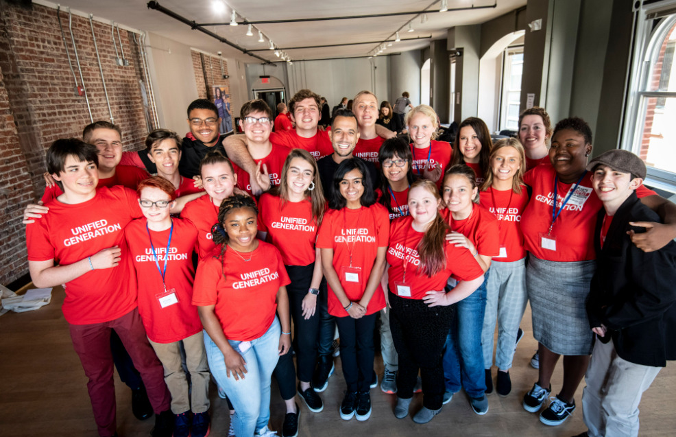A group of former U.S. Youth Ambassadors all in matching shirts surrounding ESPN's Tony Reali.