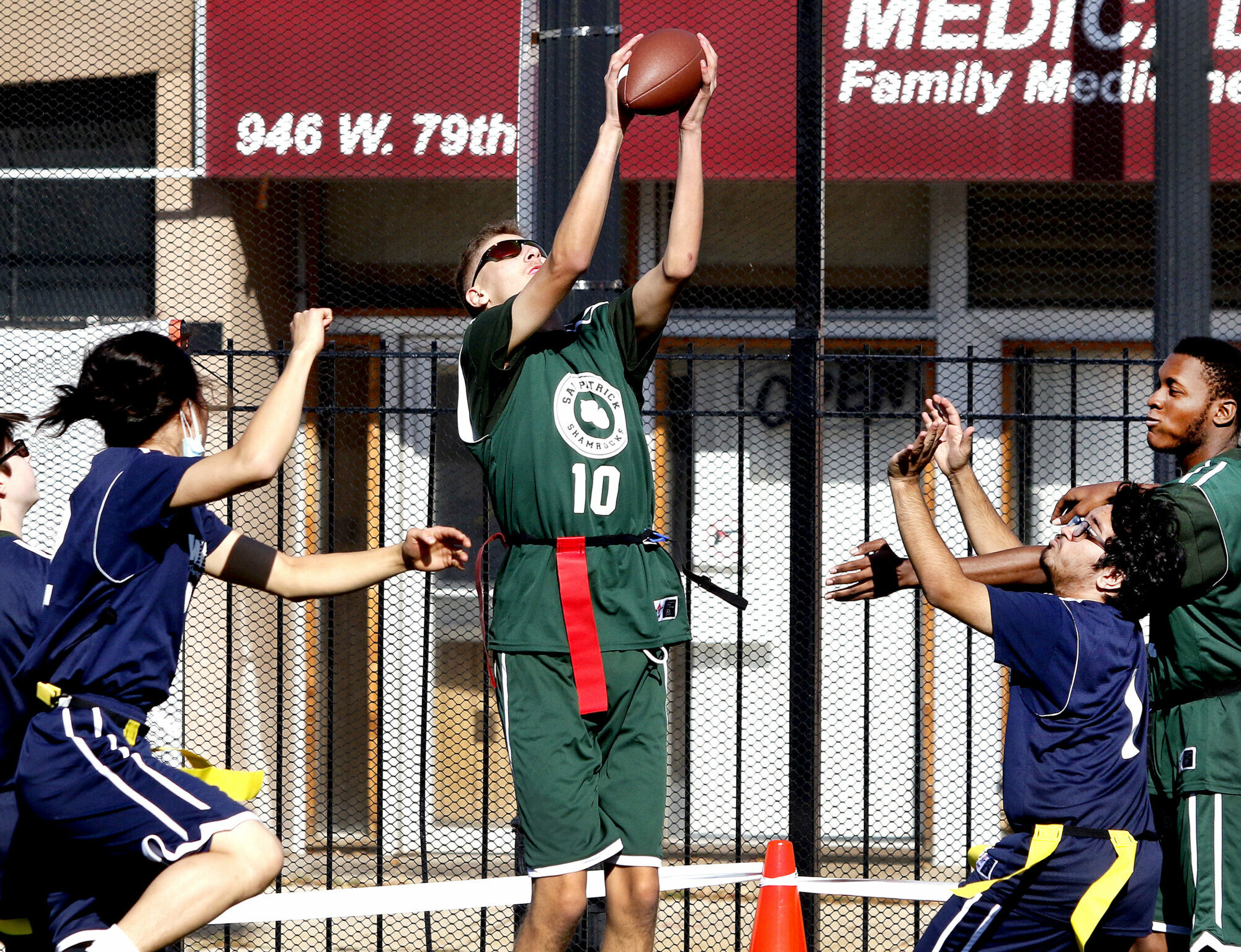 A student reaching for a football catch during a flag football scrimmage.