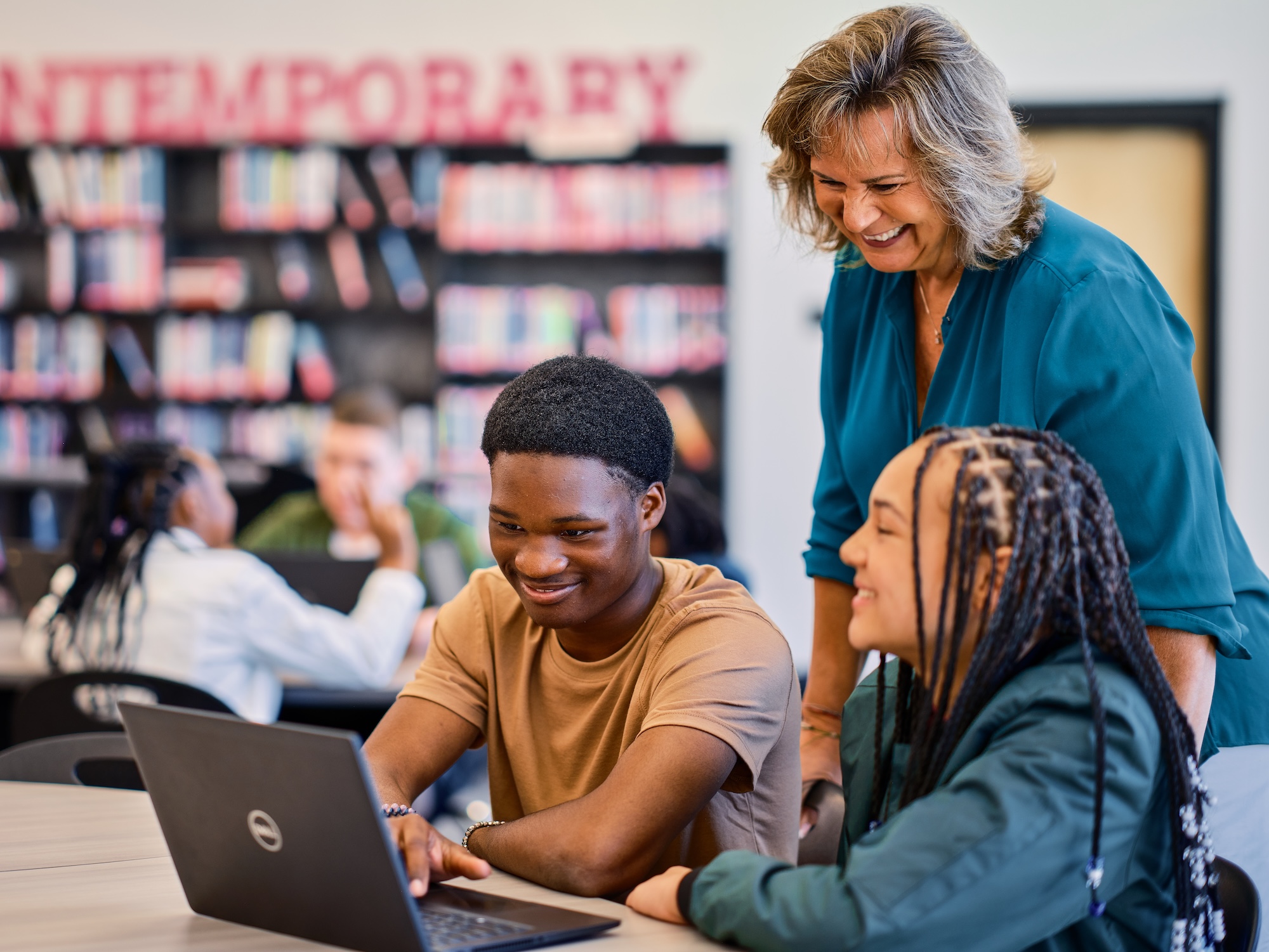 A teacher collaborates with two students as they work together on a laptop.