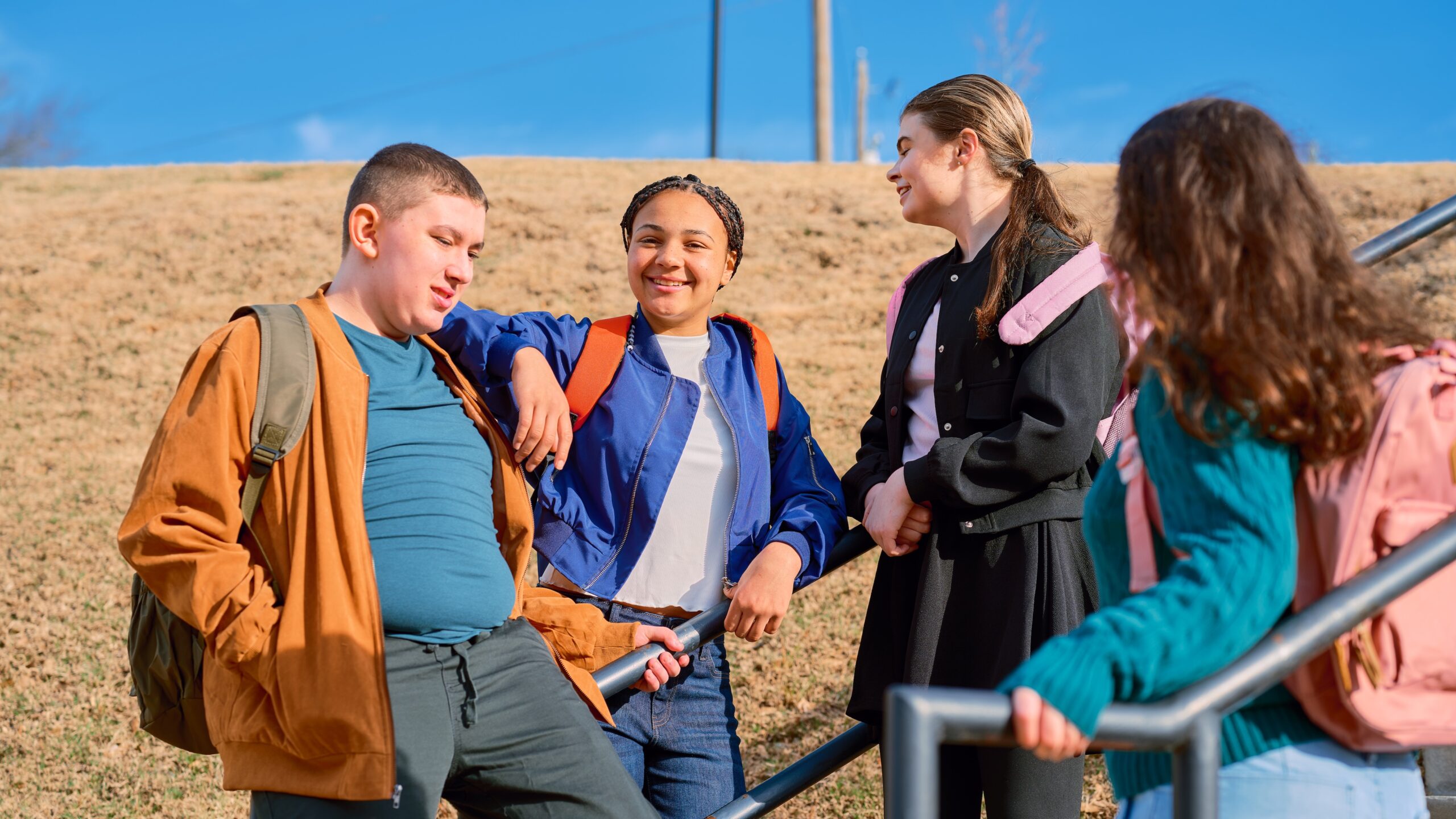 . Four young people standing together on a stairway, smiling and engaged in conversation.