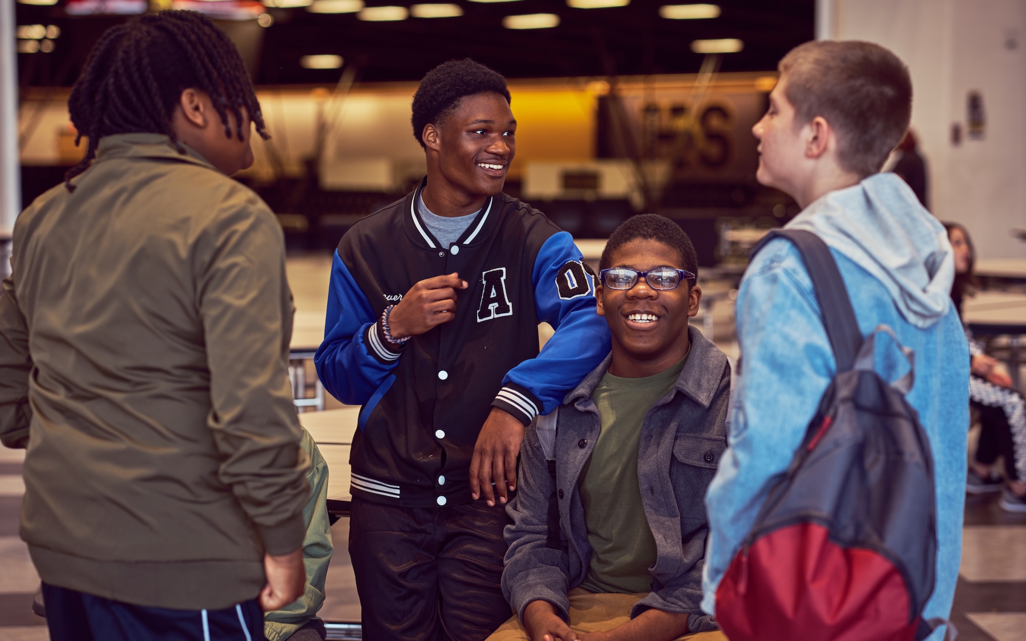 Four young men engaged in conversation in a school cafeteria.