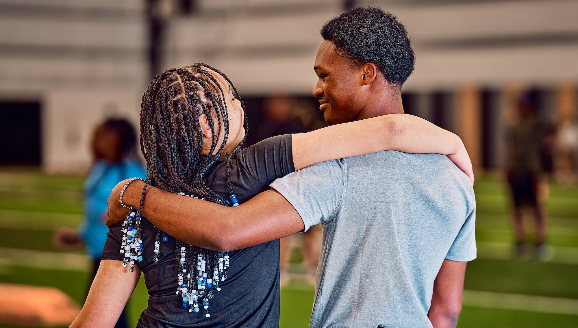 Two young people embrace each other warmly in a gymnasium.